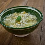 Bol de soupe Makhlouta fumante, vue en angle, sur une table rustique en bois.