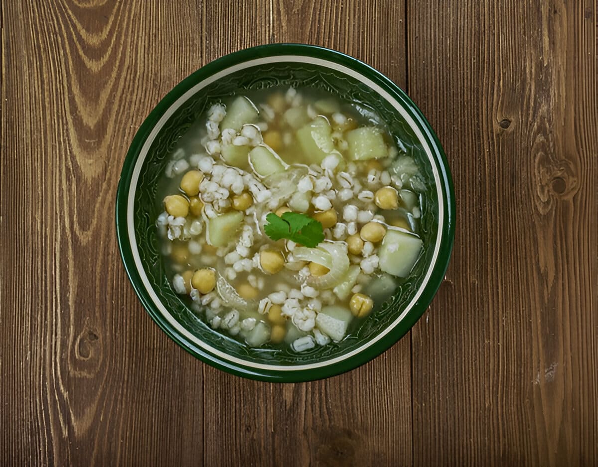 Soupe Makhlouta libanaise servie dans un bol vert Bol de soupe Makhlouta vu du dessus, avec pois chiches, orge perlé et légumes dans un bouillon clair.