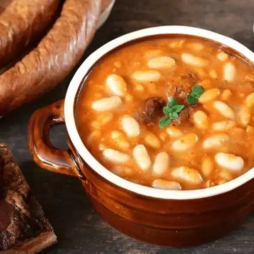 Fèves au lard servies dans un bol en terre cuite, accompagnées de viandes fumées et de saucisses.