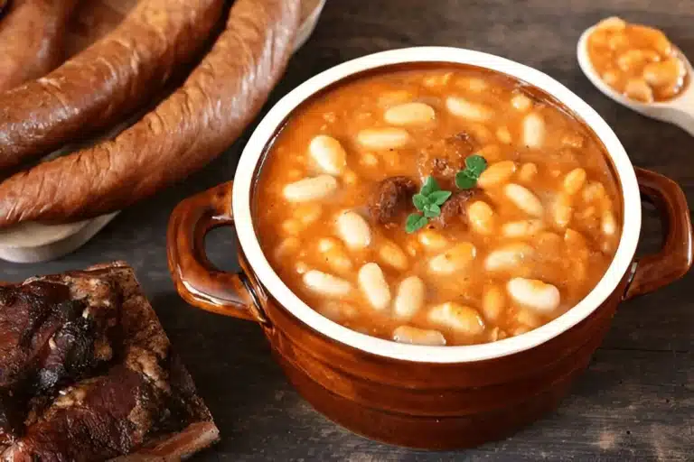Fèves au lard servies dans un bol en terre cuite, accompagnées de viandes fumées et de saucisses.