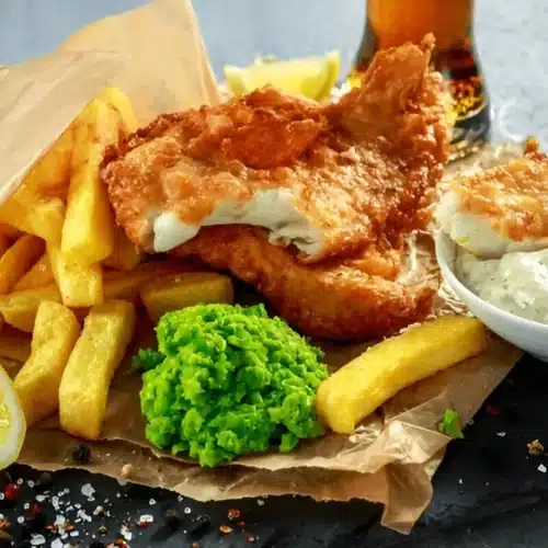 Assiette de fish and chips avec une sauce tartare, des pois écrasés et des quartiers de citron.