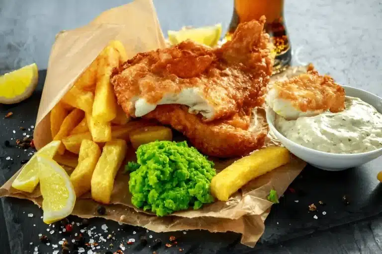 Assiette de fish and chips avec une sauce tartare, des pois écrasés et des quartiers de citron.