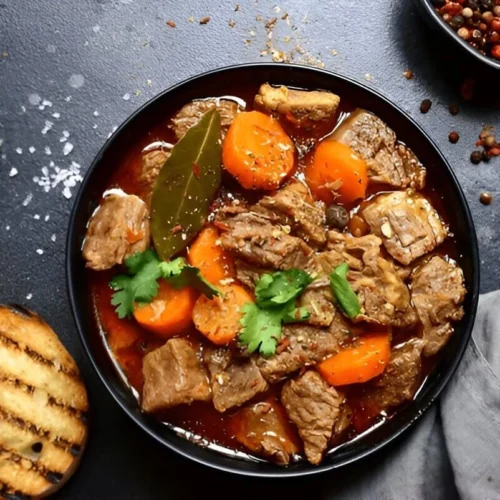 Une assiette de goulash servie avec des nouilles et parsemée de persil frais.