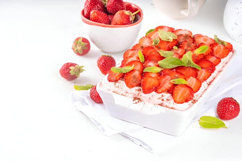Plat de tiramisu aux fraises décoré de feuilles de menthe et entouré de fraises fraîches