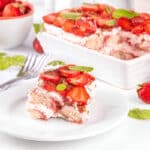 Part de tiramisu aux fraises servie sur une assiette, avec le plat complet en arrière-plan