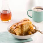 Part de pouding chômeur nappé de sirop avec une tasse de café et du sirop d’érable en arrière-plan