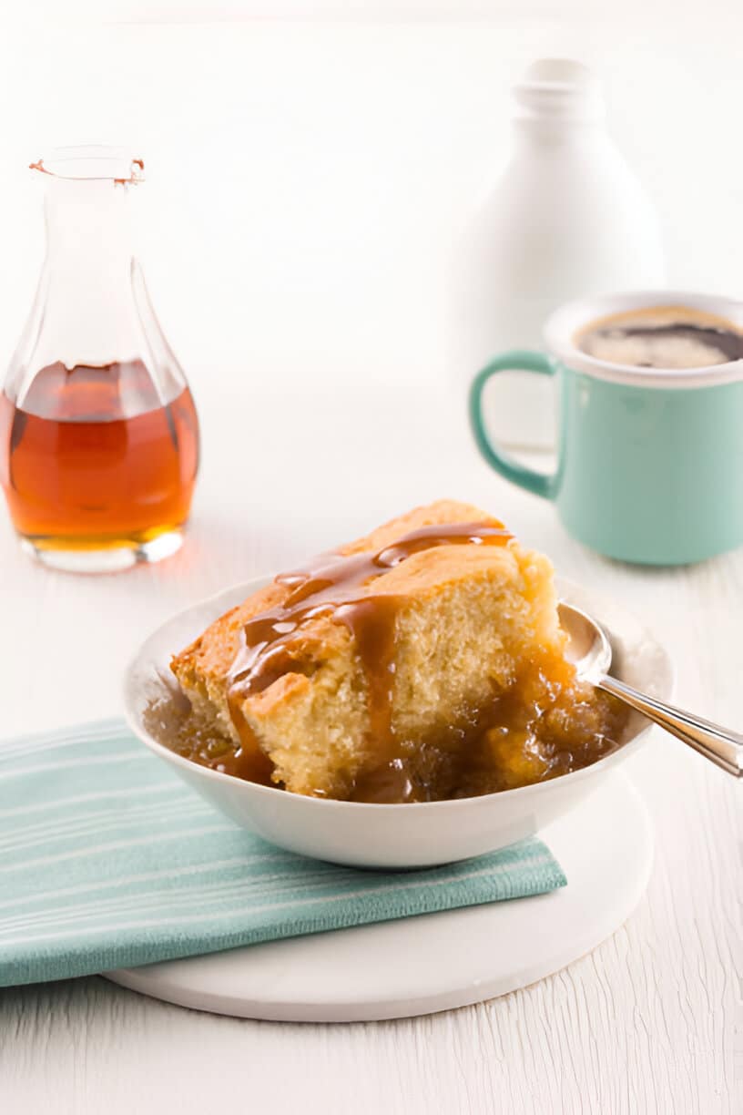 Part de pouding chômeur nappé de sirop avec une tasse de café et du sirop d’érable en arrière-plan