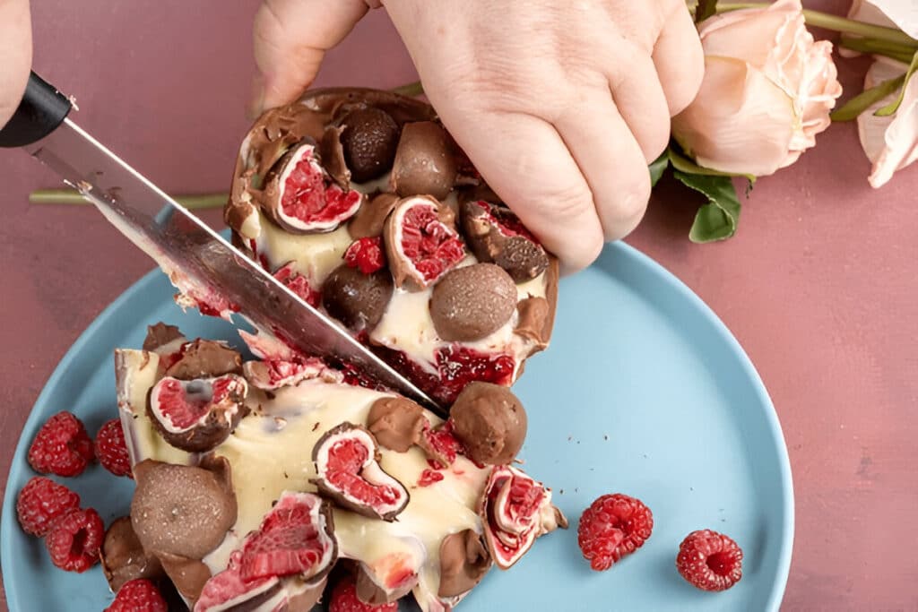 Demi-œuf en chocolat garni de framboises et truffes au chocolat, en cours de découpe.