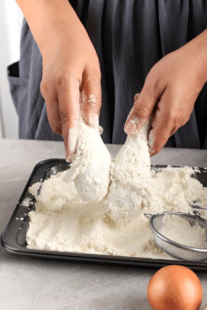 Mains plongeant du poulet dans un mélange d'œufs battus et de farine